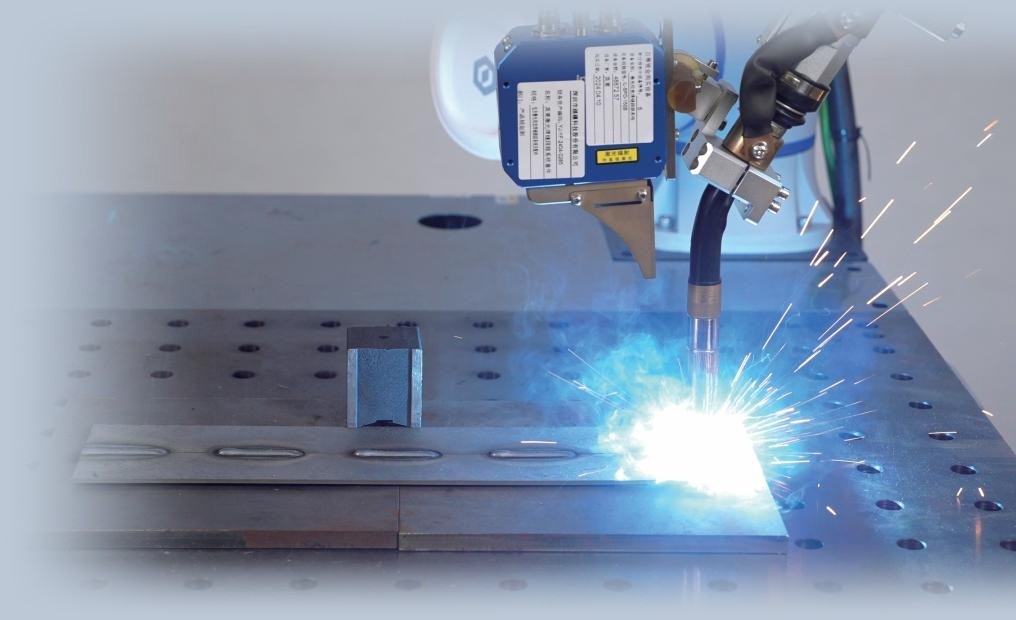 Cobot schweißt mit Lichtbogen und Funkenflug an einem Lochtisch, Laser-Sensor am Brenner